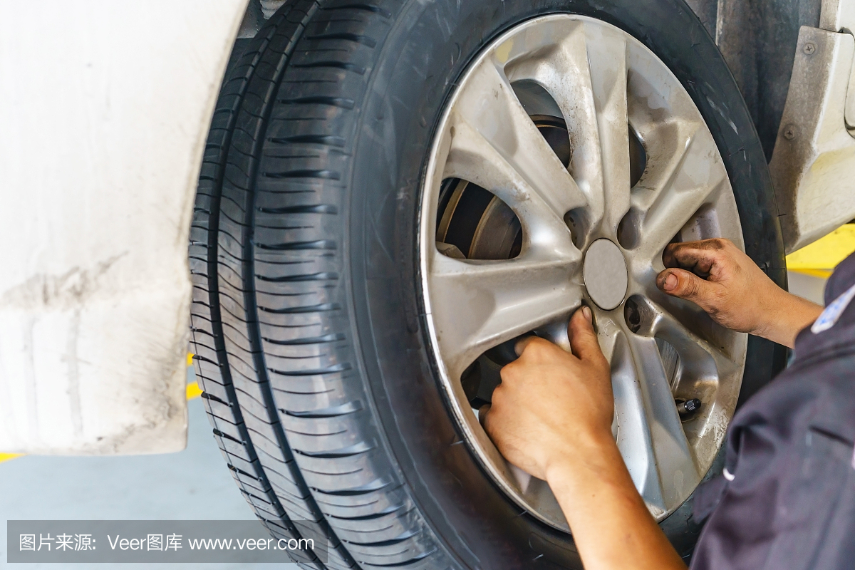 汽車服務(wù),修理,維護和人的概念-汽車技工與電動螺絲刀在車間換輪胎